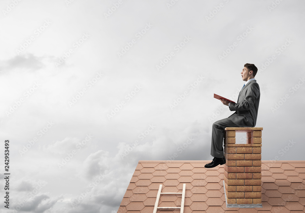 Student guy in suit on brick house roof reading book Student guy in suit on brick house roof reading book