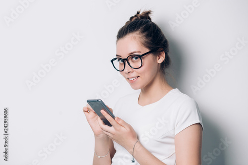 Portrait of happy smiling young woman wearing glasses using smartphone on white background