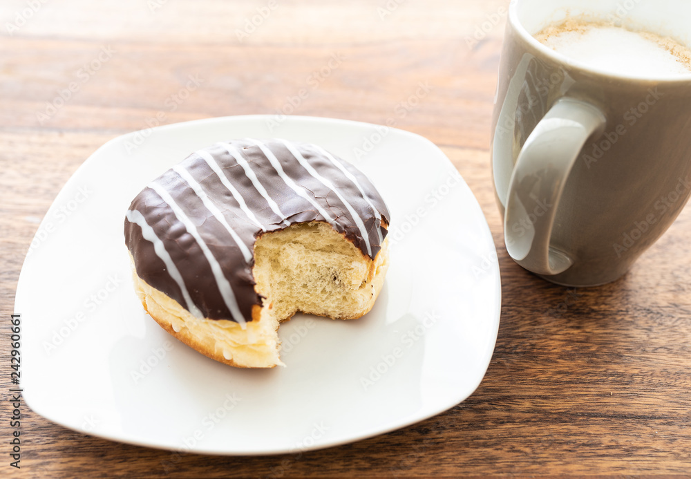high angle view of chocolate coated jelly doughnut and cup of coffee on wooden table high angle view of chocolate coated jelly doughnut and cup of coffee on wooden table