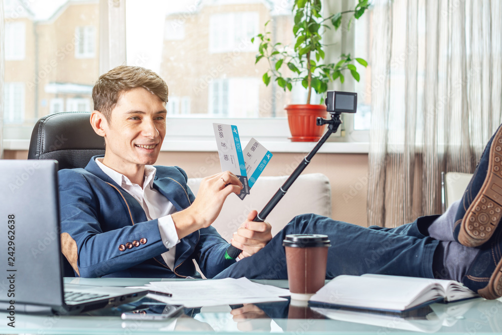 Businessman blogger with airline tickets in his hands shares joy by recording a video. Concept of the office on vacation Businessman blogger with airline tickets in his hands shares joy by recording a video. Concept of the office on vacation