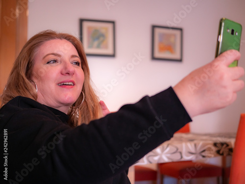 Happy woman takes a selfie photo with his mobile phone sitting on a sofa