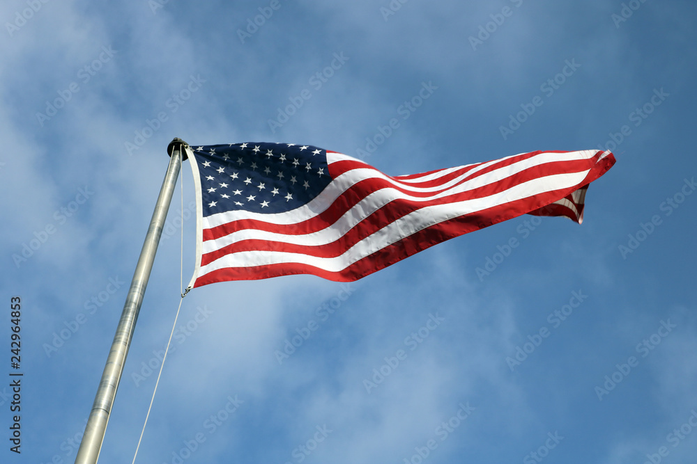 American flag on a pole flying against bright blue skies American flag on a pole flying against bright blue skies