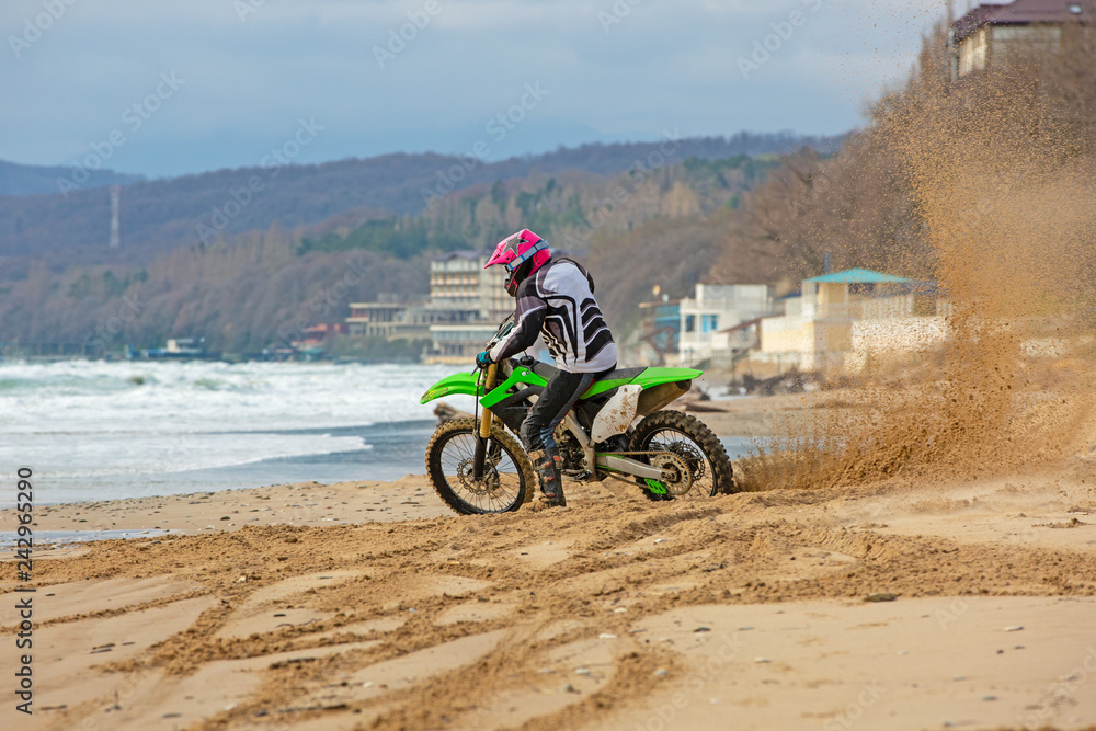 Motorcyclist in a protective suit rides a motorcycle on the sea, splashes fly from under the wheels.