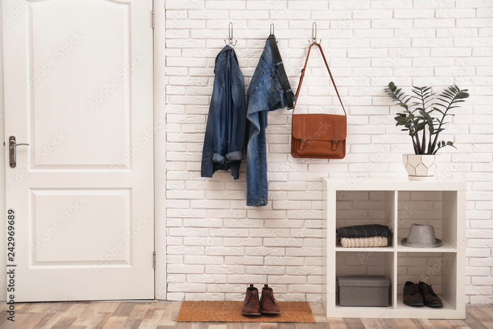 Stylish hallway interior with door, comfortable furniture and clothes on brick wall Stylish hallway interior with door, comfortable furniture and clothes on brick wall