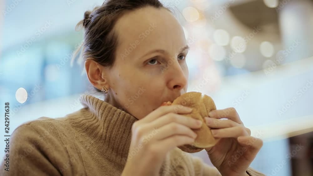 Woman biting cheeseburger at fast food restaurant. Hungry girl eating hamburger on food court. Woman biting cheeseburger at fast food restaurant. Hungry girl eating hamburger on food court.