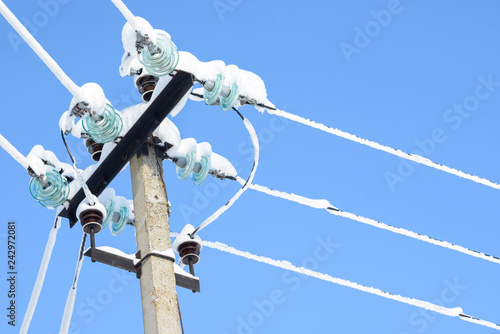 Electric communications wires covered with ice and snow. Snow-covered power cable lines and pole. Power electric transmission lines.