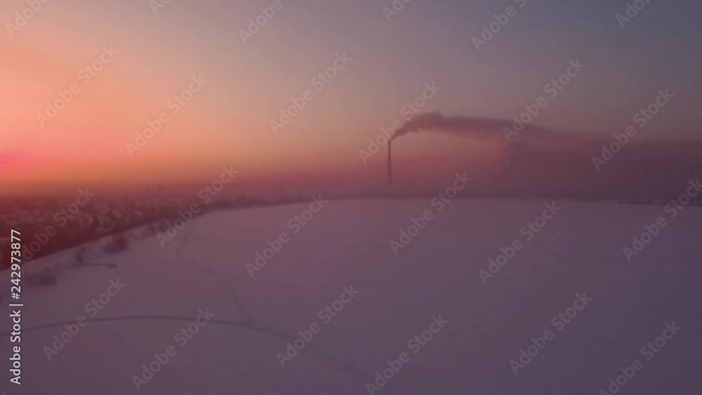 Flying over snow field sunset and lonely chimney-stalk with smoke on the horizon Flying over snow field sunset and lonely chimney-stalk with smoke on the horizon