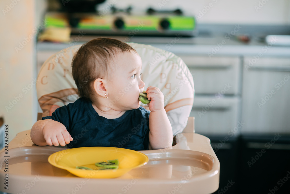 little girl on a high chair eating kiwi little girl on a high chair eating kiwi