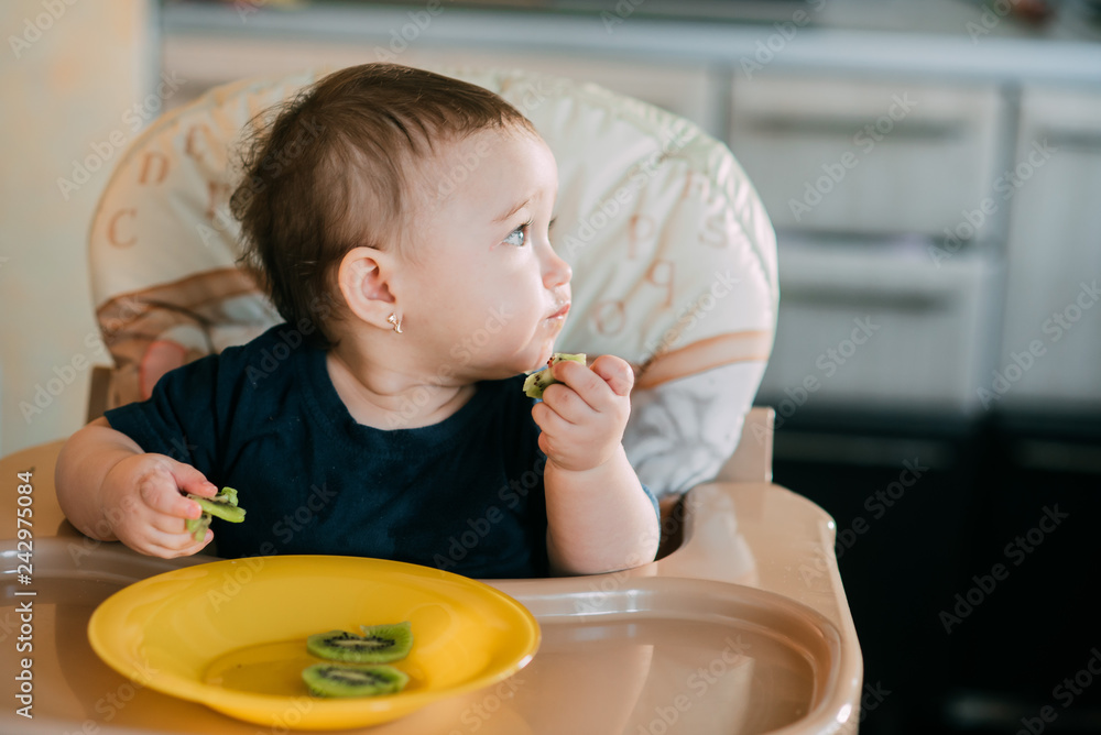 little girl on a high chair eating kiwi little girl on a high chair eating kiwi