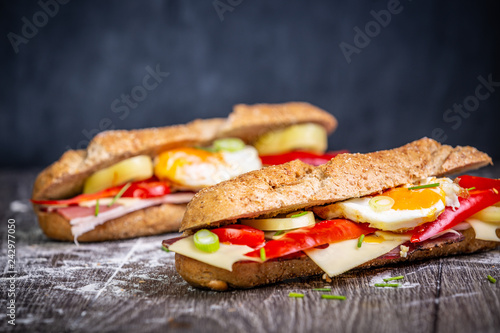 Fresh baguette sandwiches with bacon, cheese, tomatoes on wooden background