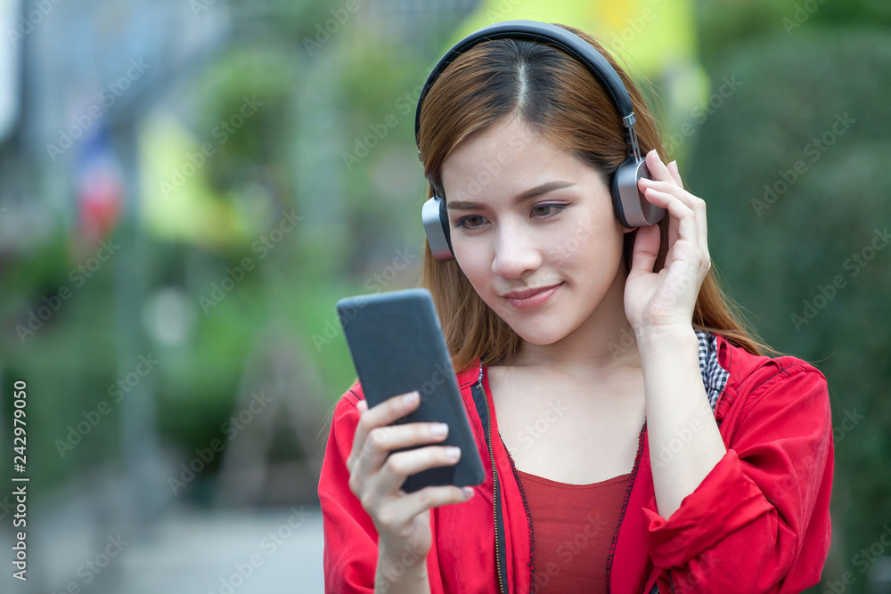 portrait of happy beautiful Young Asian women smiling in red coat listening wireless music enjoy with headphones from a smart phone on green background portrait of happy beautiful Young Asian women smiling in red coat listening wireless music enjoy with headphones from a smart phone on green background