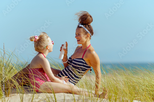 smiling mother and child on ocean coast applying sun screen photo