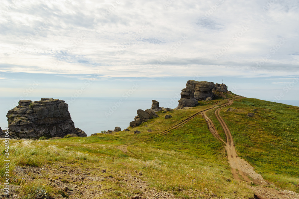 The road to the rocks in the mountains on the background of the sea and cloudy sky at the daytime.