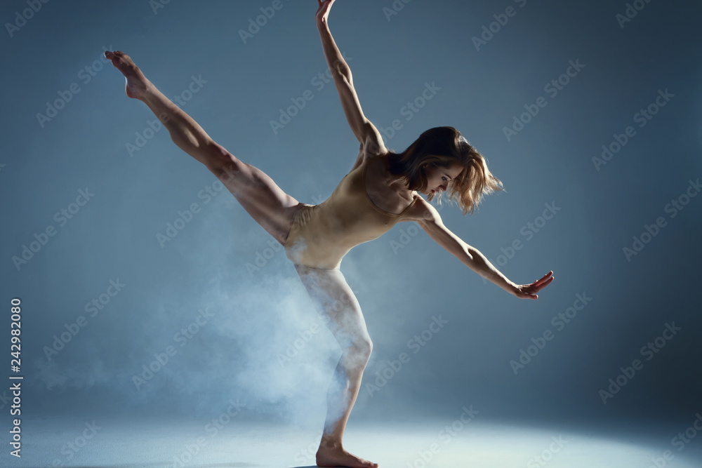Dancing in cloud concept. Muscle brunette beauty female girl adult woman dancer athlete in fog smoke dust wearing dance bodysuit making stretches dance element performance on isolated grey background
