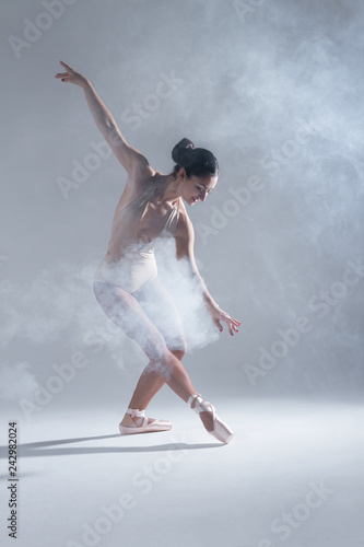 Elegant woman female girl ballerina dancer in beige body pointe shoes dancing, making performance and dance element in fog dust smoke fume on isolated grey background scene. Dancing in cloud concept