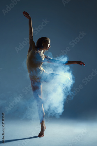 Dancing in cloud concept. Muscle brunette beauty female girl adult woman dancer athlete in fog smoke fume wearing dance bodysuit making emotional dance element performance on isolated grey background