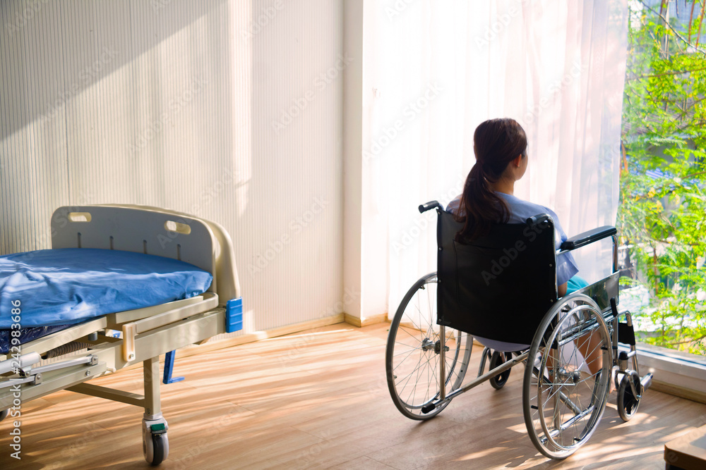 The woman sitting on wheelchair. She is see window with patient bed in hospital. The woman sitting on wheelchair. She is see window with patient bed in hospital.