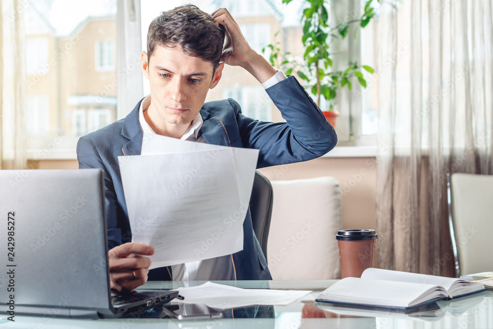 Businessman sitting at a work place examing documents. Concept of the office working with documents Businessman sitting at a work place examing documents. Concept of the office working with documents