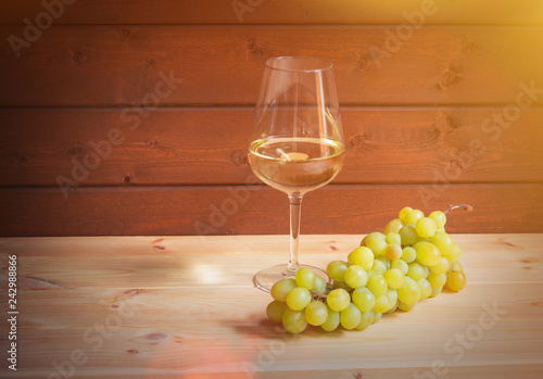 Glass of white wine and green grape branch on wooden table. View with copy space.