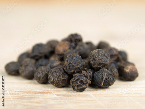 A pile of black pepper grains on a wooden plank.
