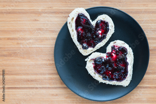 Heart shaped toasts on a plate over wooden background, top view