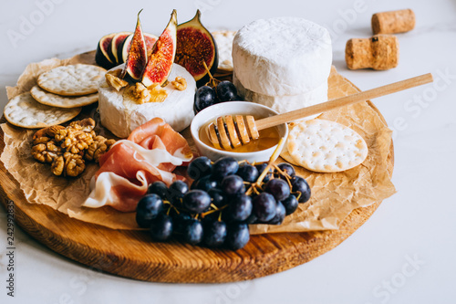 Camembert cheese, figs, jamon, honey and grapes. Cheese plate on marble background