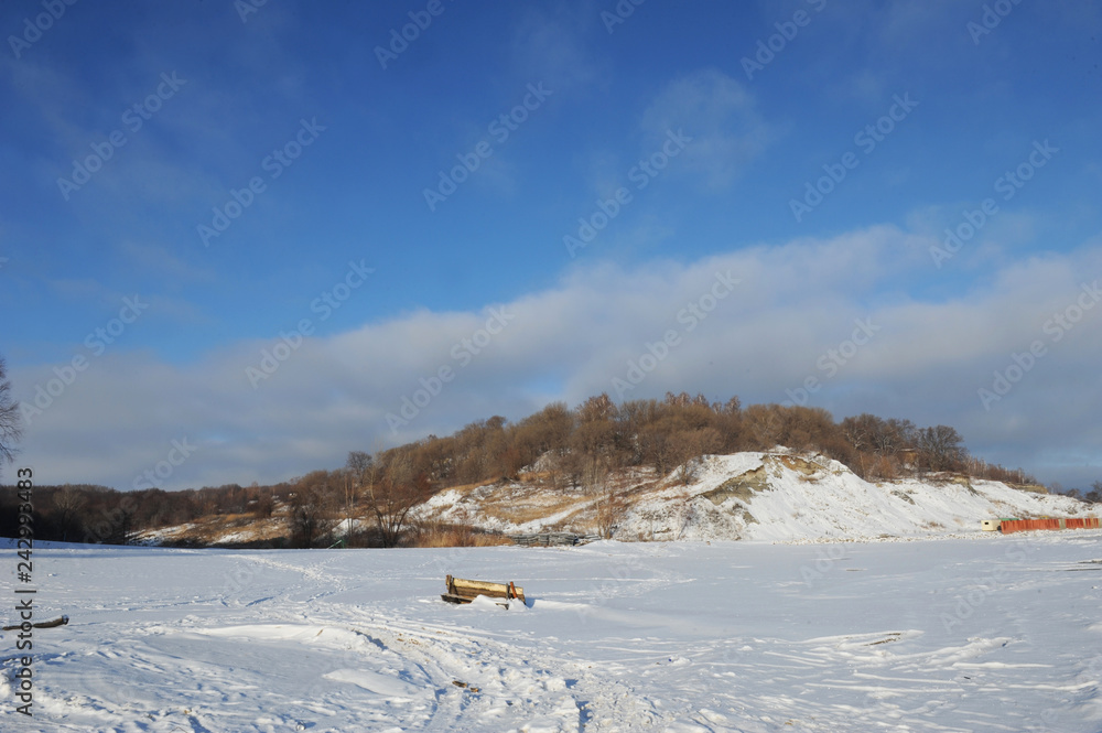 Winter snowy coastal landscape on a sunny day. Frozen river. Clear sky. Open space. Two boats on the shore