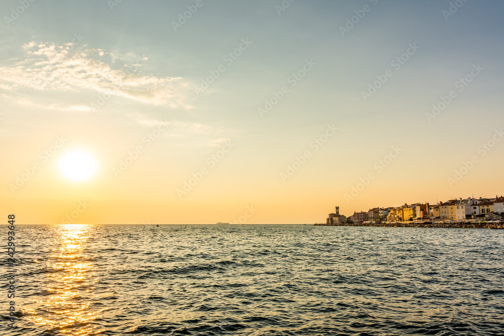 Sunset above the adriatic sea in Piran city, Slovenia. Old ancient and mediaveal city, view from coast and harbor. Old stones in foreground, beautiful clouds on sky, romantic sunset above city.