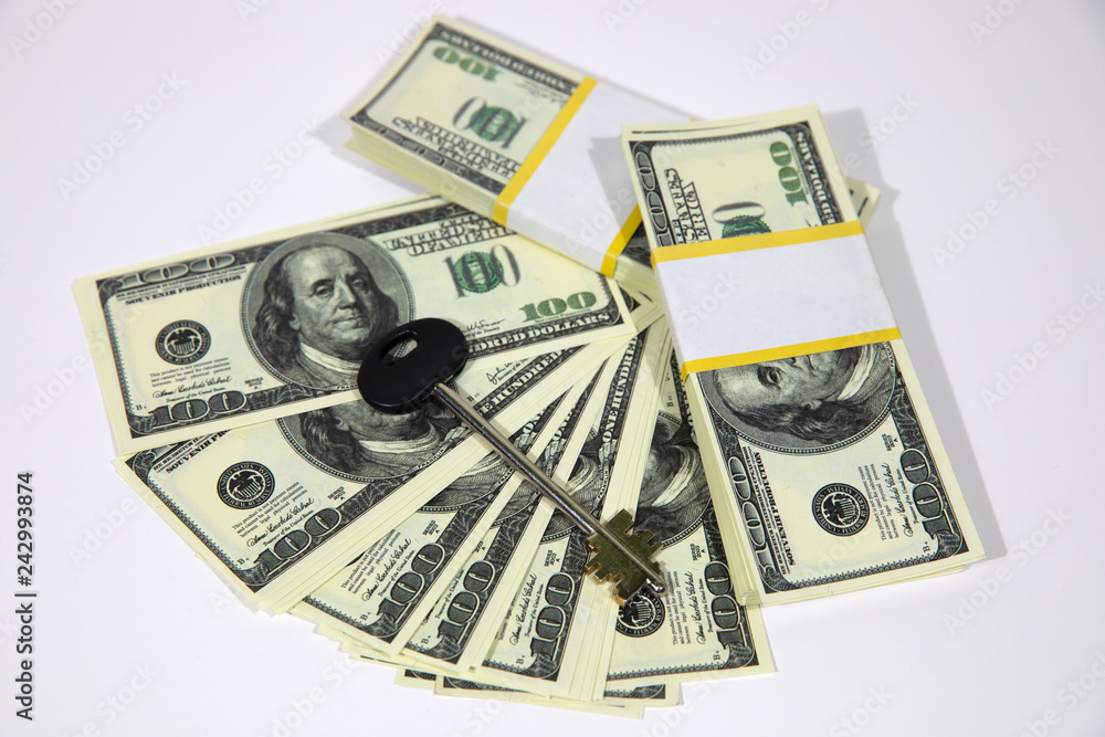 Fototapeta premium Bundles of hundred dollar banknotes on a white background. House keys. The keys to the apartment on the dollars.