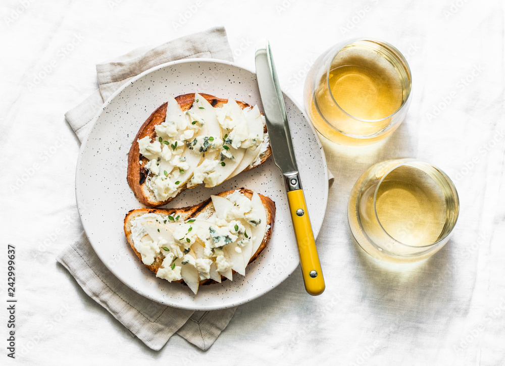 Pear, blue cheese, thyme sandwiches and white wine - delicious aperitif on a light background, top view