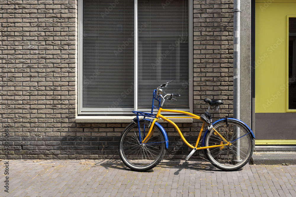 The yellow bike is parked against the wall of a brick building.