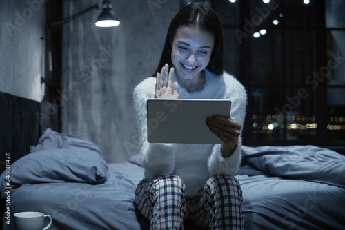 Foto Photo of young woman sitting on bed with tablet communicating via video chat