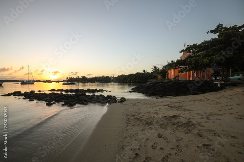 Sunset on the beach of the island of Mauritius where yachts float on water and there is a house