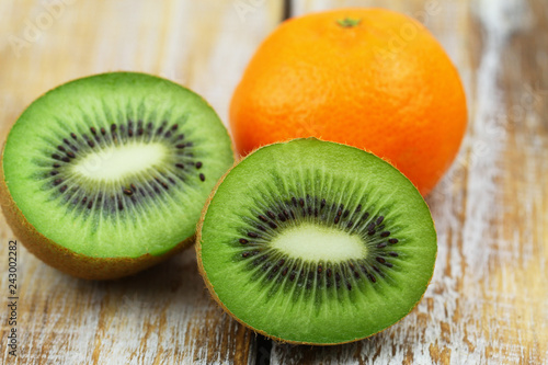 Closeup of two halves of fresh kiwi fruit and orange on rustic wooden surface

