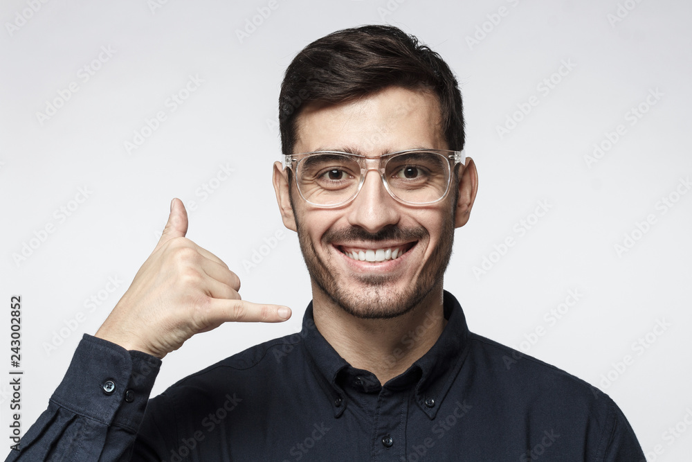 Young man showing gesture as if asking to calll him, looking confident, isolated on gray background. Technical support concept Young man showing gesture as if asking to calll him, looking confident, isolated on gray background. Technical support concept
