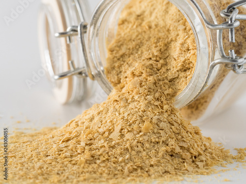Nutritional yeast background. Nutritional inactive yeast spilled from glass jar on white background. Copy space.Side view.Nutritional yeast is vegetarian superfood with cheese flavor, for healthy diet
