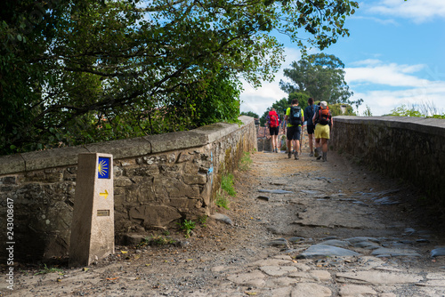 FURELOS, SPAIN - JULY 31, 2016: Some young pilgrims with backpacks cross a medieval bridge, making the Camino de Santiago. photo