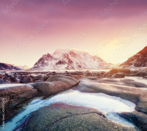 Mountains, stone, water and sunrise on Lofoten islands, Norway. Natural landscape in the Norway. Sunrise on the seashore and reflection on the water surface