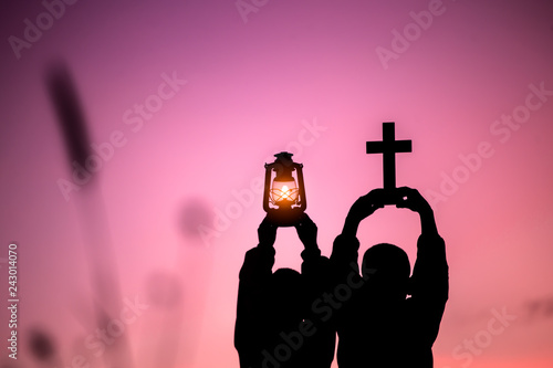 Two children holding oil lamp and cross with light sunset background,christian concept.