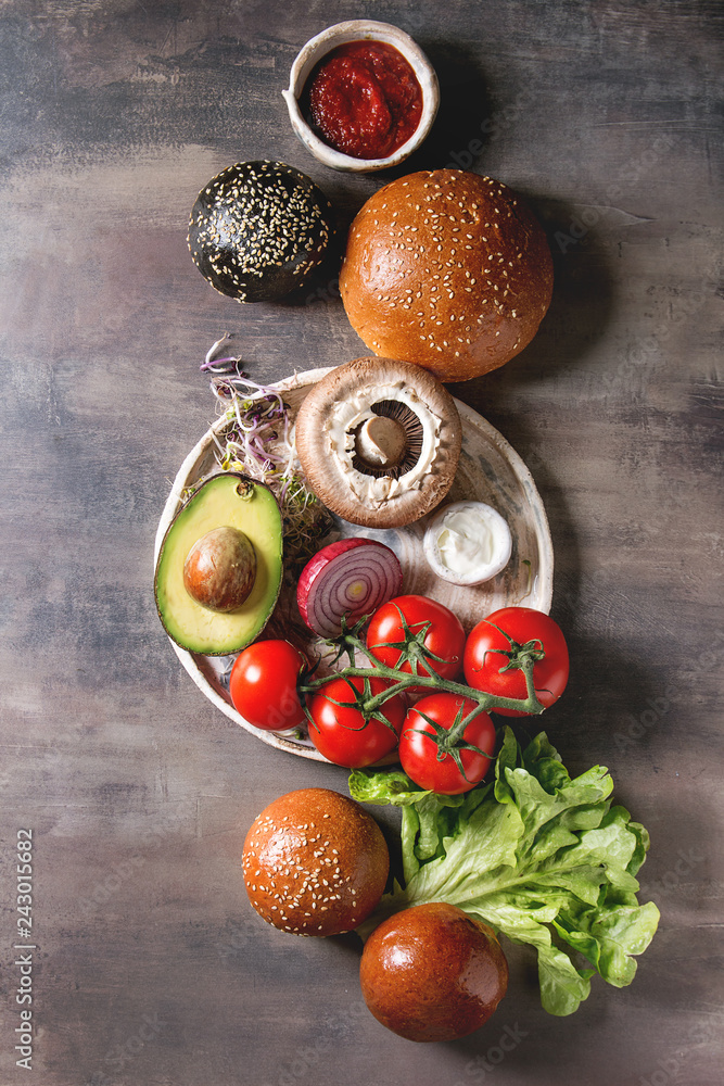 Ingredients for cooking homemade vegan hamburgers. Cheese, avocado, portobello mushroom, tomato, green sprouts, black and white buns, salad, onion. Dark background. Top view, space.