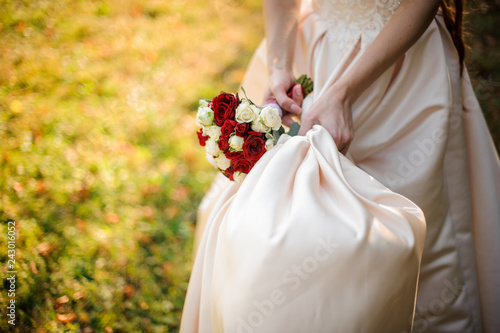 Bride hand holding a wedding dress and bouquet of flowers