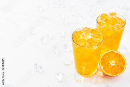 Fresh orange juice in tall glass with orange and ice on white marble table. Copy space for text. Summer drink. Horizontal.