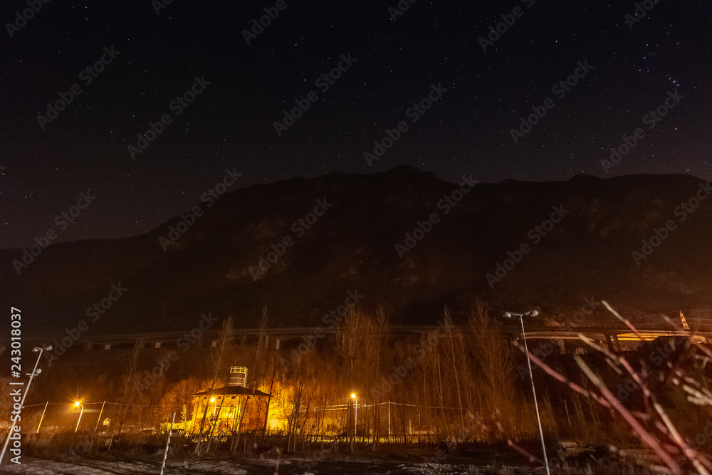 Starry sky above a valley, with houses illuminated at the foot of the mountain, Vittorio veneto, Italy
