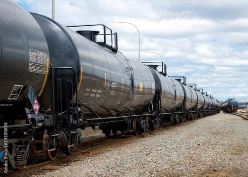 Black railway tanker cars of the type used to transport petroleum products. Several cars visible on two separate sets of tracks. Identification markings have been removed, only technical info remains.