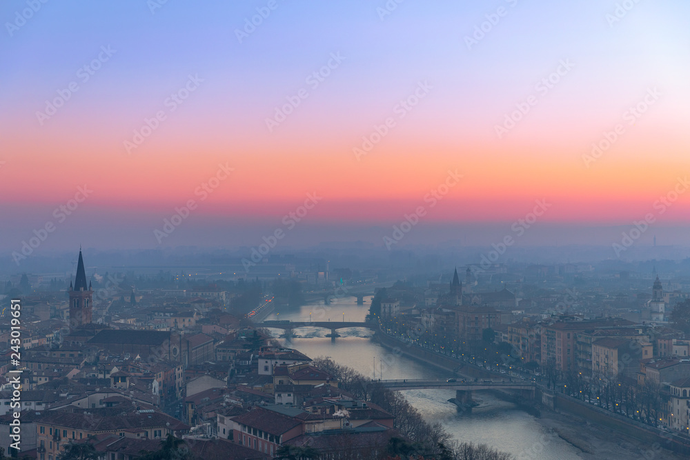 Panoramic view of the city of Verona and the Adige river with bridges covered with the evening mist colored by the setting sun. Sunset in Verona. Winter time. Italy.