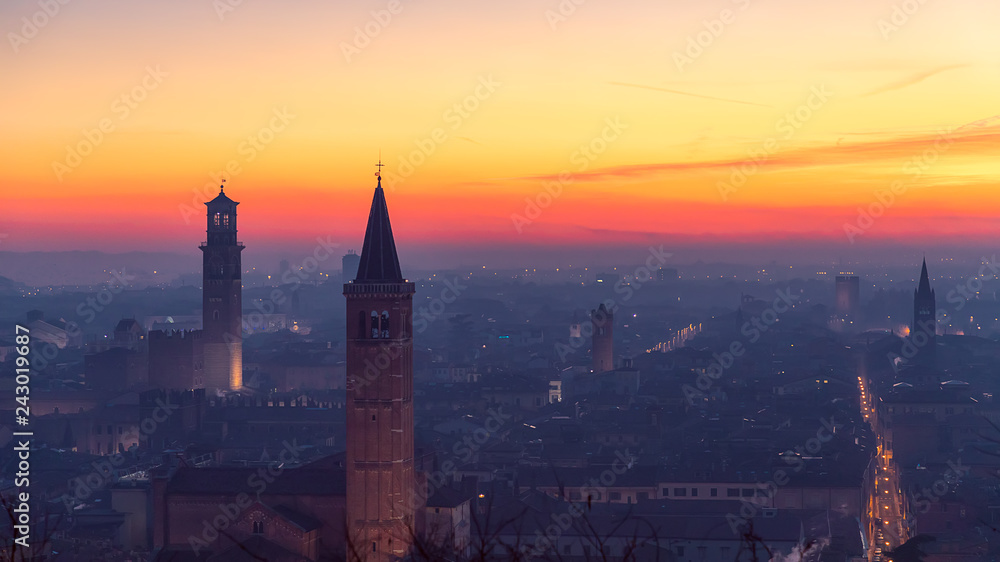Fototapeta premium Beautiful panoramic sunset view of old town of Verona, Torre Lamberti and Santa Anastasia bell tower covered with evening fog. View from Piazzale Castel S. Pietro. Winter time. Verona, Italy