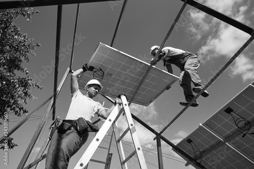 Teamwork for installing innovative solar pannels on the roof for using renewable energy resources. Envirinment friendly green energy. Economical, innovative solution for housebuilding. Black and white photo