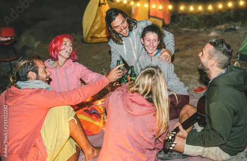 Group of friends having fun cheering with beers on the beach with tent at night - Happy young people playing guitar and laughing together - Friendship  Vacation and camping lifestyle concept
