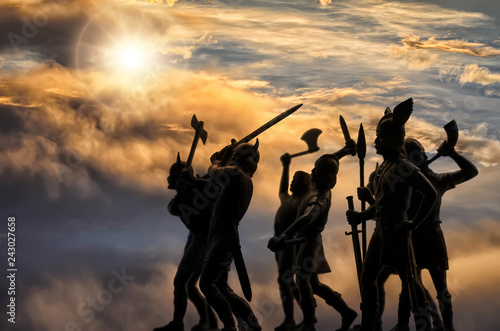 Dark silhouettes of well armed attacking Vikings against the sky with thunder clouds and bright sunshine, Old Norse mythology, Odin, Valhalla and Asgard themes