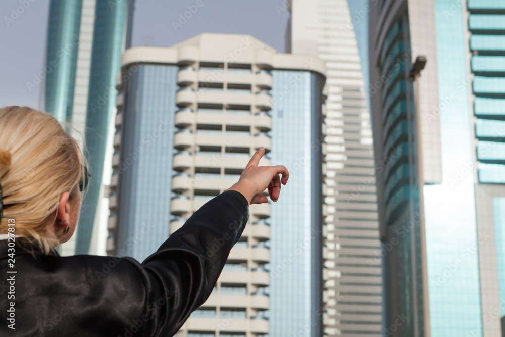 Rear view of businesswoman,pointing on a skyscraper,cityscape in the background Rear view of businesswoman,pointing on a skyscraper,cityscape in the background